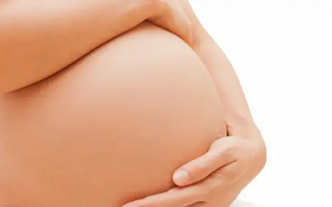 Dłoń obejmuje ciążowy brzuch. Zaparcia w ciąży to częsty problem, ale można sobie z nimi radzić.