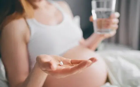 Kobieta w ciąży trzyma tabletkę i szklankę wody. Dba o siebie, przyjmując rutinoscorbin w ciąży.