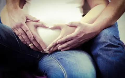 Dłonie tworzą serce na brzuchu w 5 miesiącu ciąży. Czekamy na nasze maleństwo.