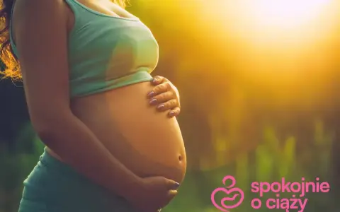Brzuszek w 3 miesiącu ciąży, otulony ciepłym światłem. Ręce delikatnie go obejmują, symbolizując troskę i miłość.