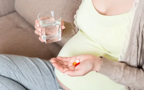 Kobieta w ciąży bierze suplementy, w tym magnez, popijając wodą. Dba o zdrowie swoje i dziecka.