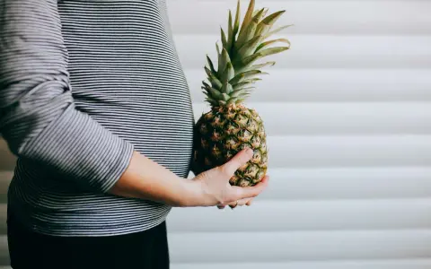 Brzuch kobiety w paski, trzymająca ananasa. Wygląda jak ananas w ciąży, symbolizujący zdrową dietę.