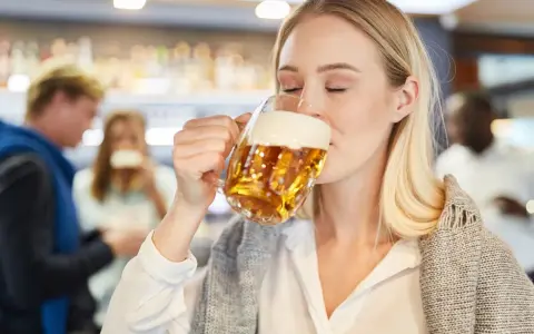 Kobieta z zamkniętymi oczami pije piwo bezalkoholowe w ciąży, ciesząc się smakiem w pubie.