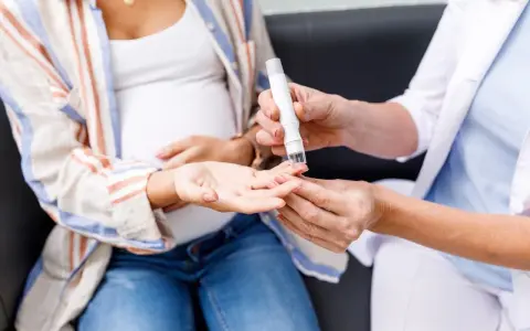 Badanie krzywej cukrowej w ciąży. Lekarz pobiera próbkę krwi z palca ciężarnej kobiety.
