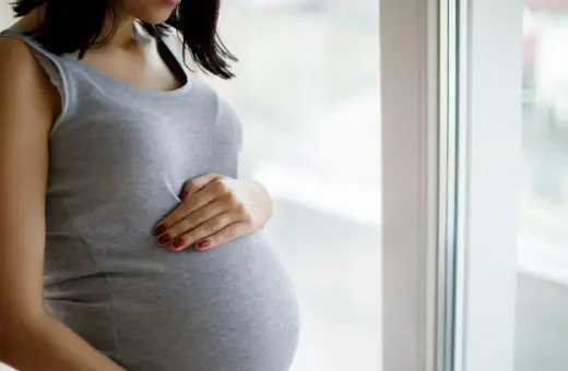 Kobieta w ciąży, która czeka na poród, delikatnie dotyka brzucha. Może to być związane z ćwiczeniami na wywołanie porodu.