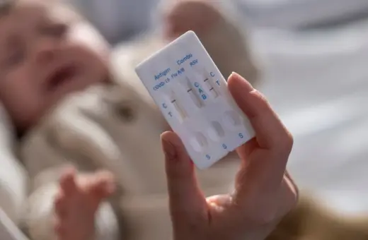 Dłoń trzyma test combo na COVID-19, grypę i RSV. W tle niewyraźne dziecko.