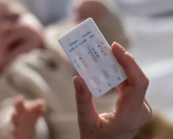 Dłoń trzyma test combo na COVID-19, grypę i RSV. W tle niewyraźne dziecko.