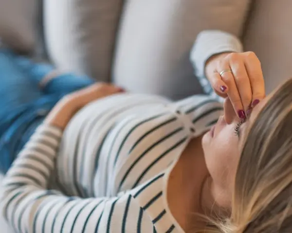 Kobieta w ciąży leży na kanapie, dotykając czoła. Zmartwienie o brak bicia serca w 8 tygodniu ciąży maluje się na jej twarzy.