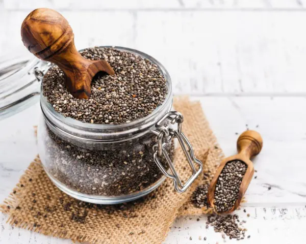 Słoik pełen nasion chia, idealnych dla kobiet w ciąży, z drewnianą łyżką. Nasiona chia to bogactwo kwasów omega-3 i błonnika.