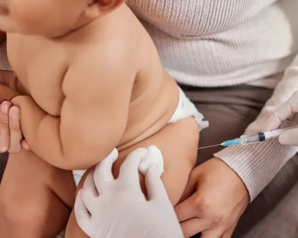Dziecko otrzymuje szczepienie. Ręka w rękawiczce trzyma strzykawkę, a druga ręka przygotowuje miejsce wkłucia. To ważny moment dla zdrowia, jak w przypadku szczepionki heine medina.