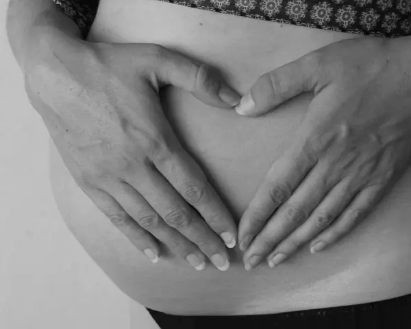 Dłonie tworzą serce na brzuchu ciężarnej. Intensywne ruchy dziecka mogą być sygnałem niedotlenienia.