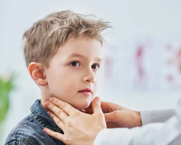 Lekarz bada szyję chłopca, sprawdzając, czy nie ma powiększonych węzłów chłonnych u dzieci. Zdjęcia takie pokazują ważny element diagnostyki.
