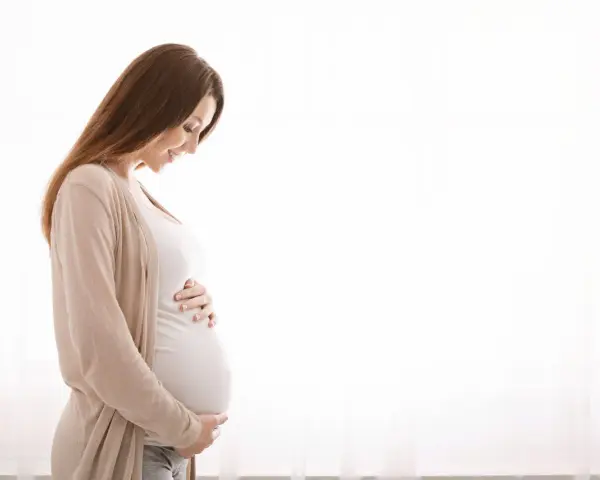 Kobieta w ciąży z hashimoto delikatnie dotyka brzucha, patrząc na niego z miłością.