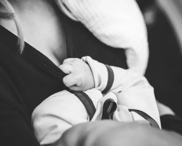 Dłoń noworodka chwyta ubranie mamy. Delikatne paluszki, które mogą wywołać **baby blues**, ale też ogromną miłość.