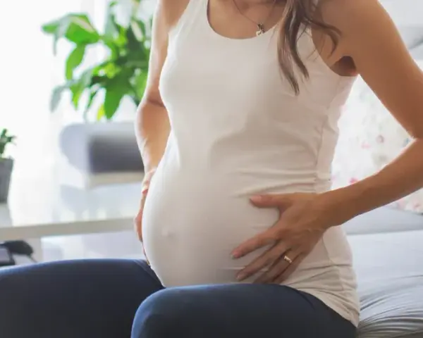 Kobieta w ciąży siedzi na kanapie, dotykając brzucha. Zauważyła brązowe plamienie w ciąży, co ją martwi.