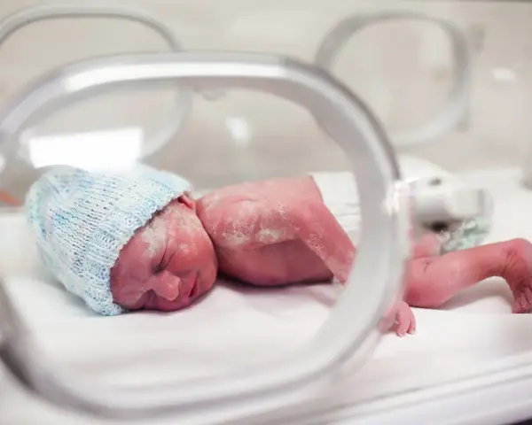 Maleńki noworodek w niebieskiej czapeczce leży w inkubatorze. To dziecko urodzone w 20 tygodniu ciąży, walczące o życie.