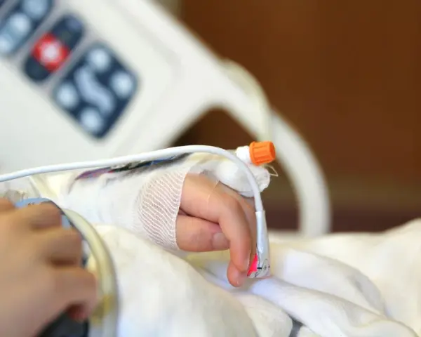 Dziecko z zespołem westa w szpitalu, z wenflonem w dłoni i czujnikiem pulsoksymetru.