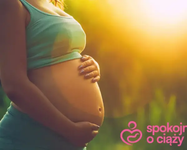 Brzuszek w 3 miesiącu ciąży, otulony ciepłym światłem. Ręce delikatnie go obejmują, symbolizując troskę i miłość.