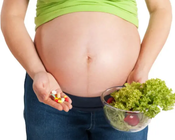 Kobieta w ciąży trzyma garść tabletek i miskę sałatki. Ważne jest żelazo dla kobiet w ciąży, czy wybrać suplementy czy zdrową dietę?