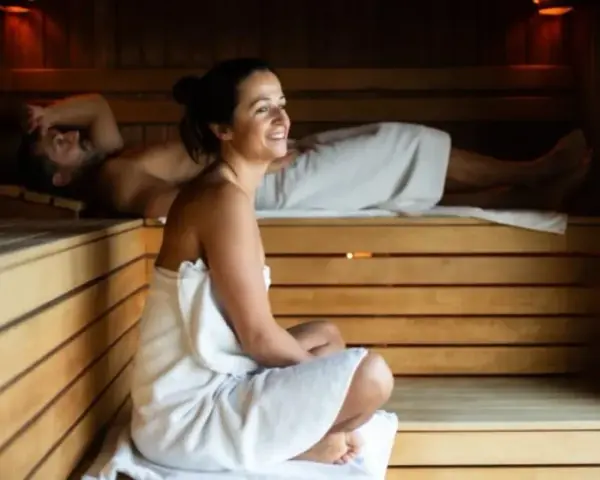 Para relaksu w saunie. Kobieta w ciąży i mężczyzna odpoczywają w drewnianej saunie, otuleni ręcznikami.