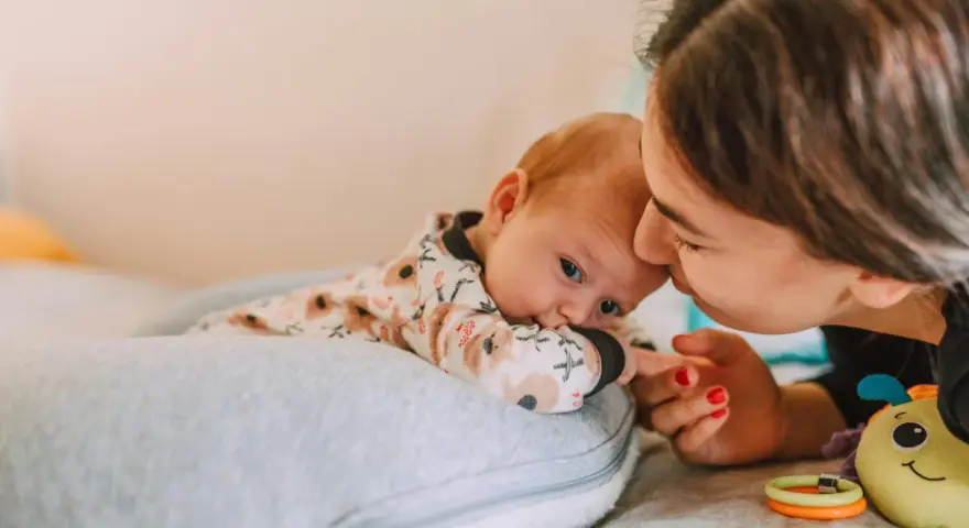Mama pochyla się nad dzieckiem, które leży na poduszce. Szybki oddech u noworodka może być naturalny, ale czujność rodzica jest ważna.