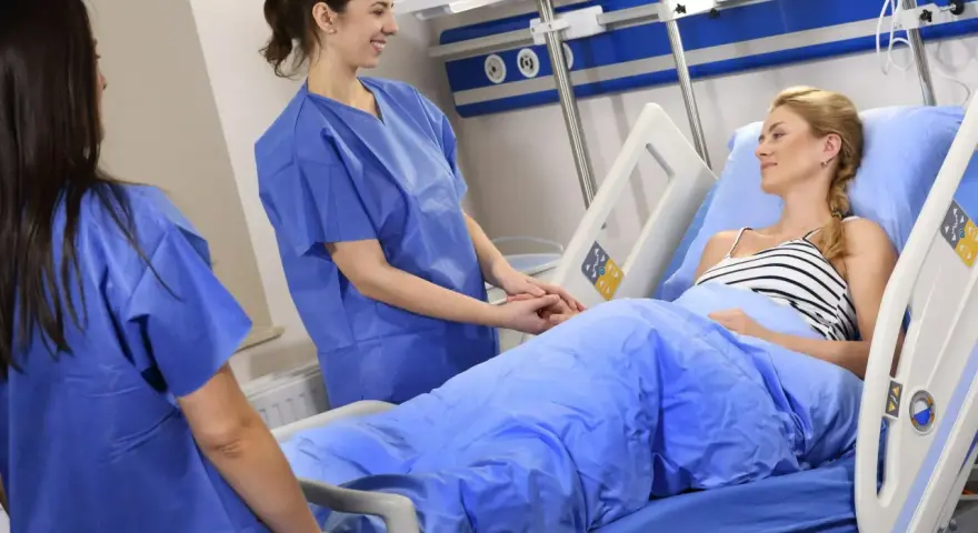 Dwie pielęgniarki w niebieskich fartuchach troskliwie opiekują się pacjentką w łóżku szpitalnym. Czy to CMV?