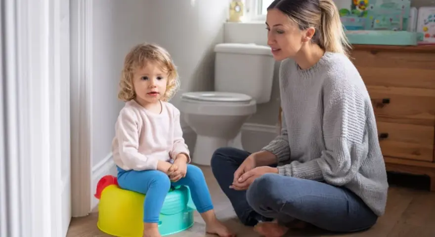 Mama uczy dziecko, jak nauczyć dziecko korzystać z nocnika. Maluch siedzi na kolorowym nocniku, mama siedzi obok.