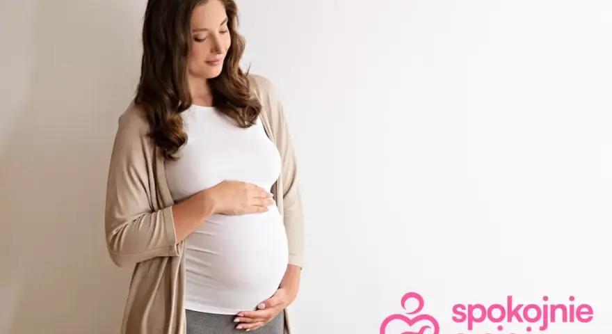 Kobieta w 29 tygodniu ciąży, z dłońmi na brzuchu, patrzy z miłością na swoje dziecko.