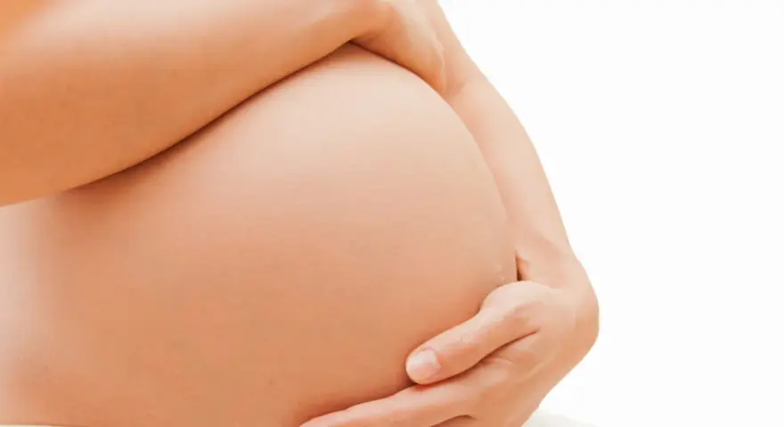 Dłoń obejmuje ciążowy brzuch. Zaparcia w ciąży to częsty problem, ale można sobie z nimi radzić.
