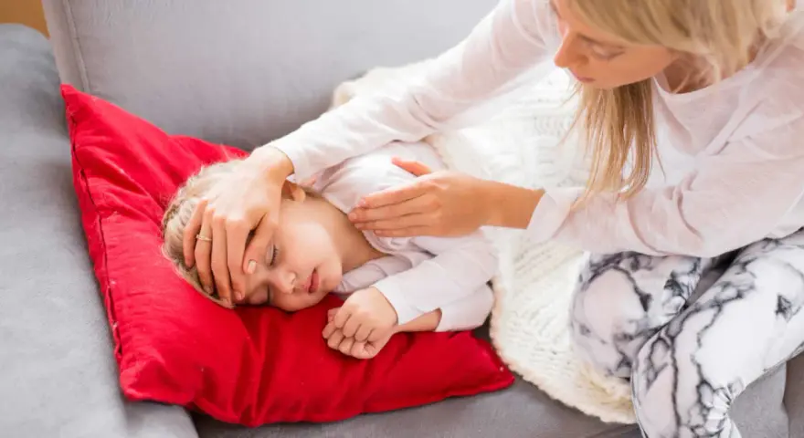 Matka sprawdza czoło śpiącego dziecka, które ma niską temperaturę.