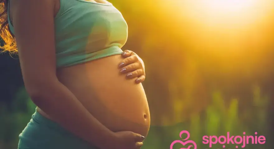 Brzuszek w 3 miesiącu ciąży, otulony ciepłym światłem. Ręce delikatnie go obejmują, symbolizując troskę i miłość.