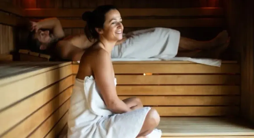 Para relaksu w saunie. Kobieta w ciąży i mężczyzna odpoczywają w drewnianej saunie, otuleni ręcznikami.