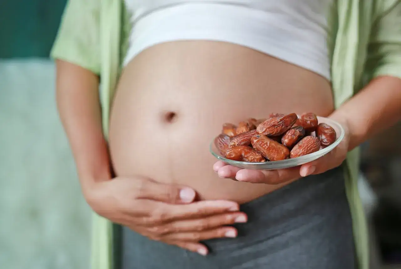 Brzuch kobiety w ciąży, trzymającej talerzyk z daktylami. Zdrowa dieta w ciąży to podstawa.
