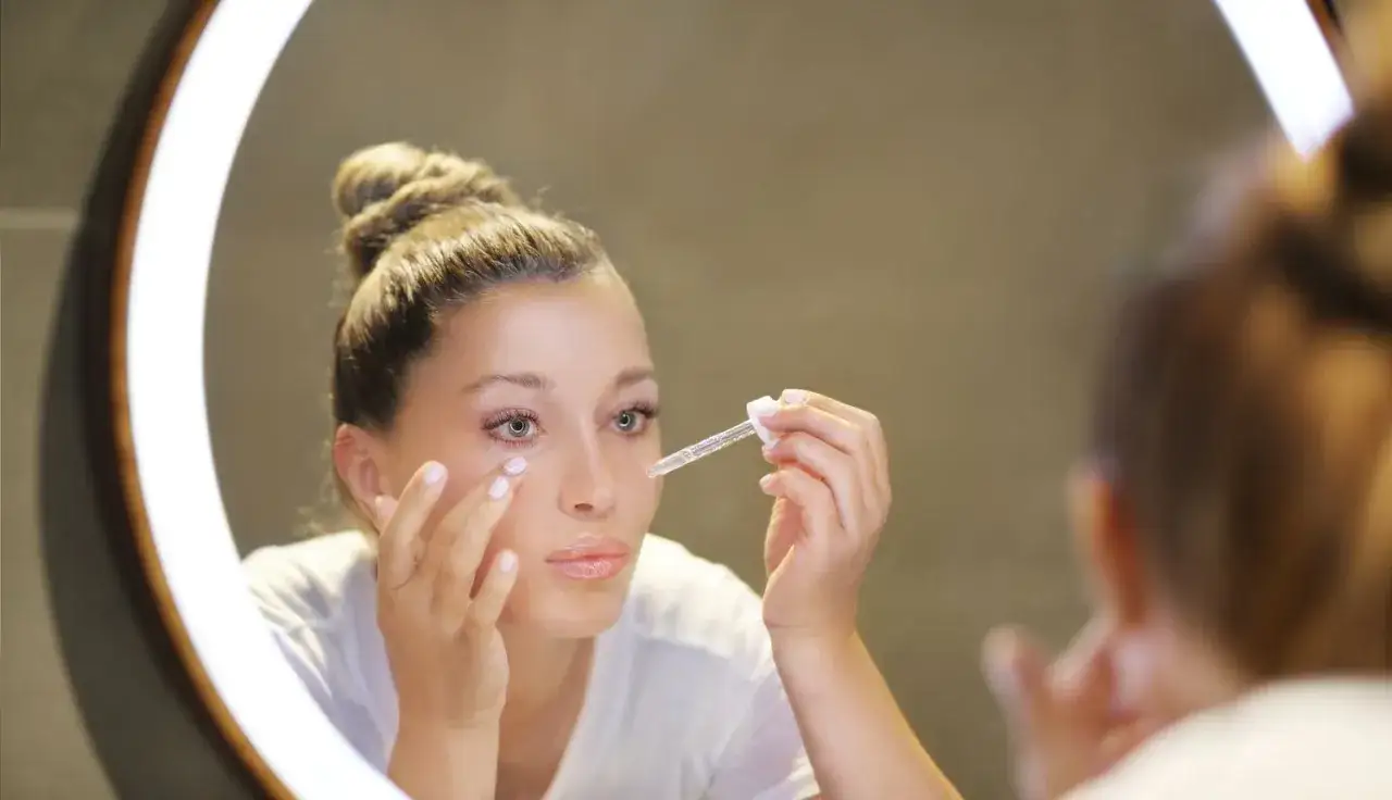 Kobieta w ciąży aplikuje serum z kwasem hialuronowym pod oczy, dbając o delikatną skórę.
