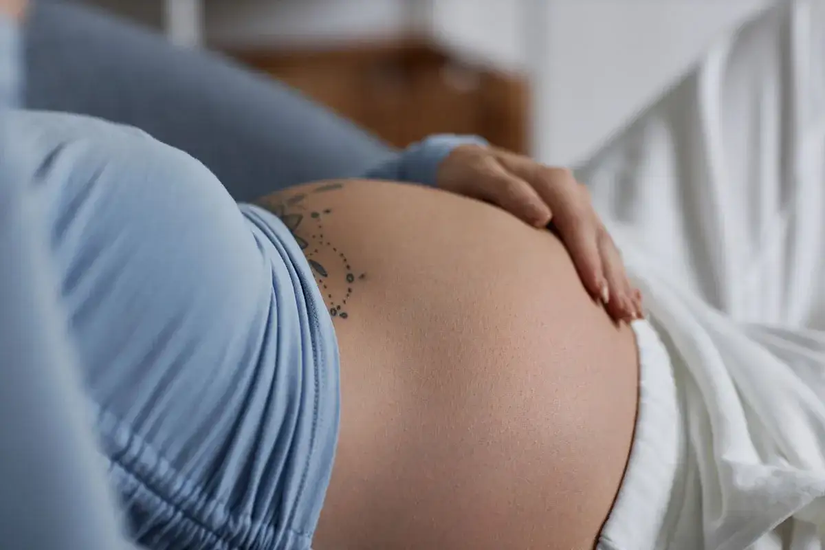 Brzuszek w ciąży, delikatny tatuaż i dłoń. Kobieta czuje się komfortowo, być może dzięki Espumisan w ciąży.