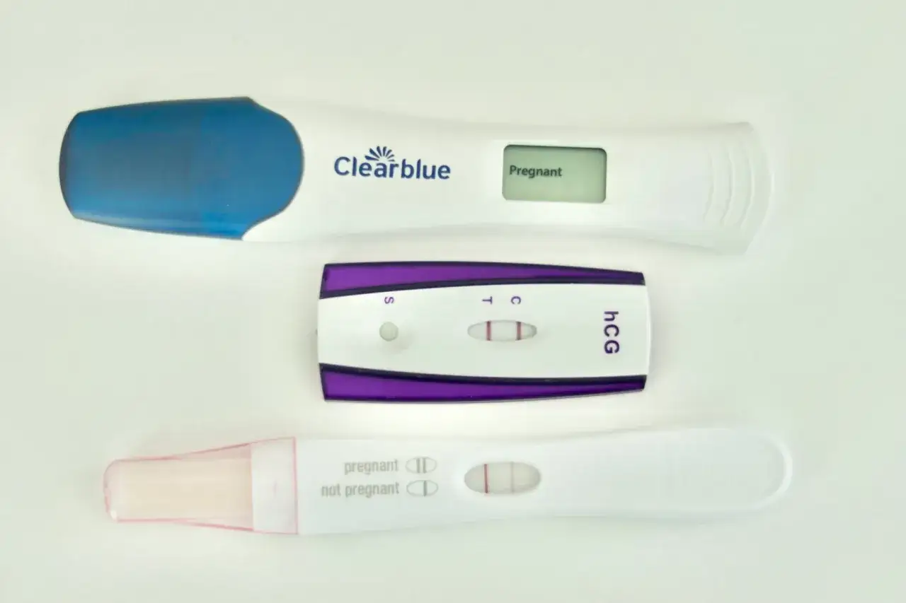 Trzy testy ciążowe, dwa z widocznymi dwoma kreskami, wskazujące na pozytywny wynik. Jeden cyfrowy Clearblue pokazuje napis 