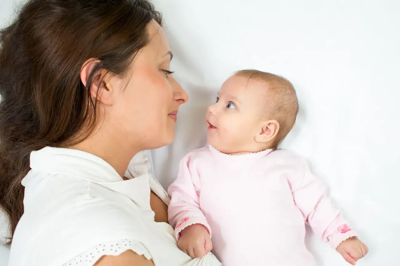 Mama patrzy z miłością na swoje 3 miesięczne dziecko, które leży na białym tle.
